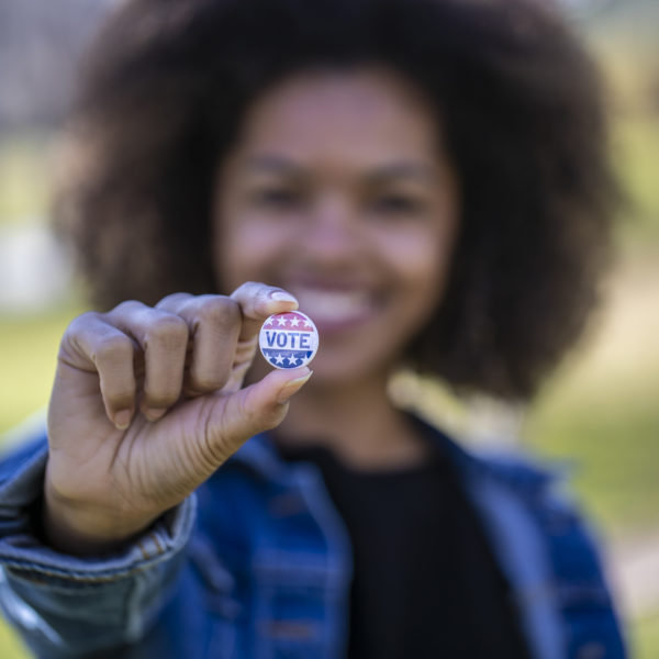 A young African American woman holding a voting badge.