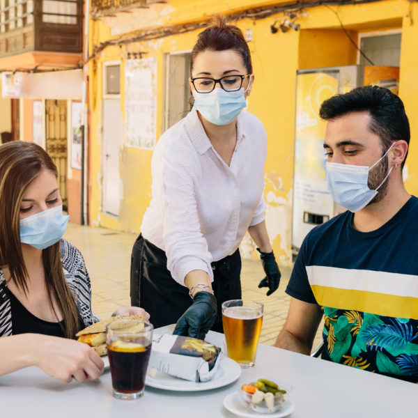 Clients with masks on the terrace of a bar in Spain attended by a waiter with gloves and masks. Social distancing